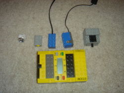 Lego Mindstorms programmable brick shown alongside three sensors (touch, light and rotation) and an electric motor.