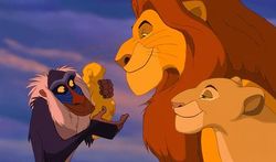 Rafiki holds Mufasa and Sarabi's newborn lion cub, Simba.